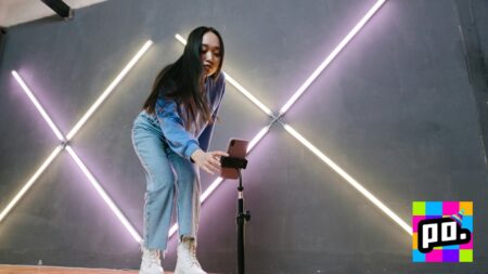 Woman holding smartphone on tripod in front of neon lights for live streaming